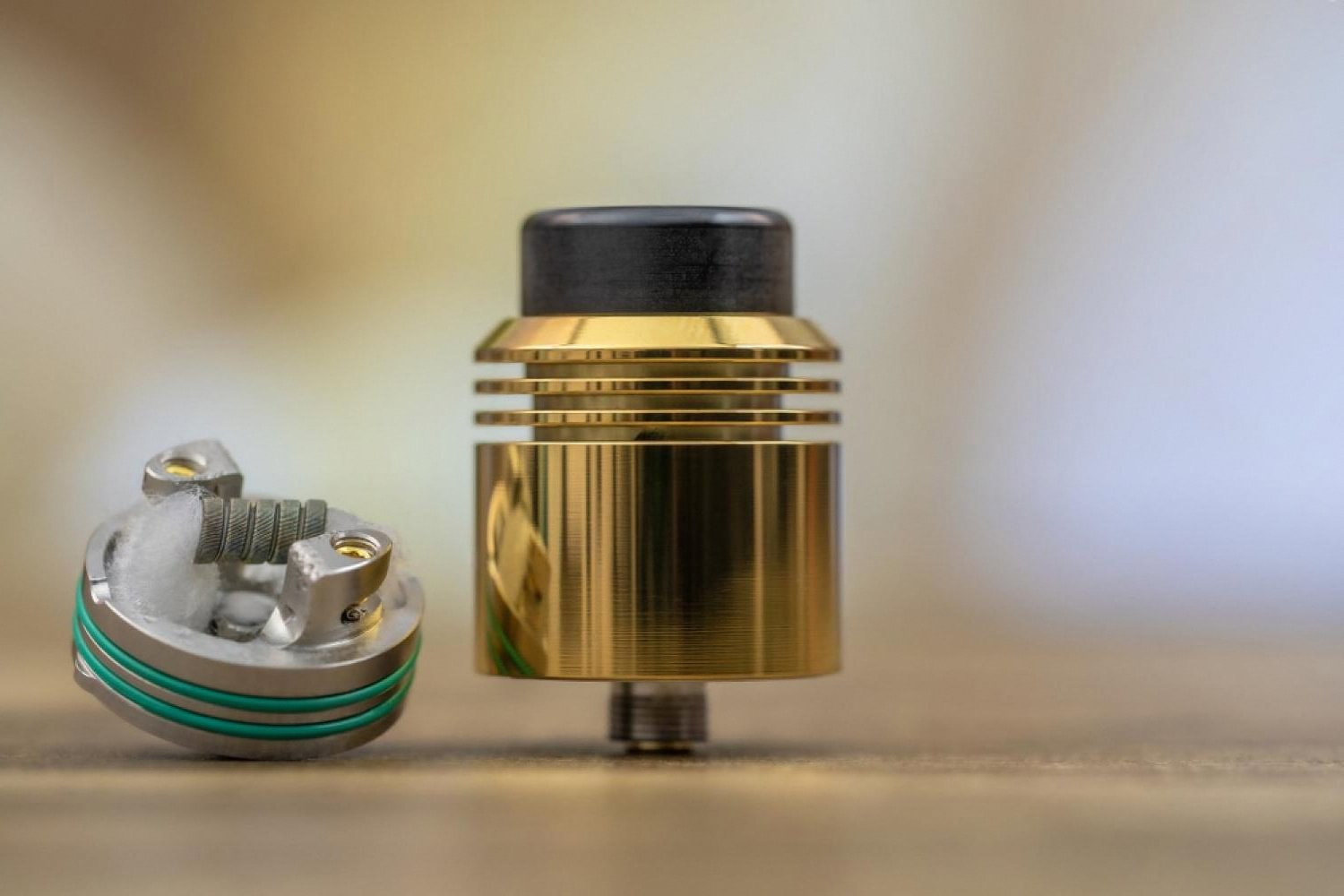 Close-up of a brass premium vape atomizer next to a stainless steel deck with a hand-built mesh coil
